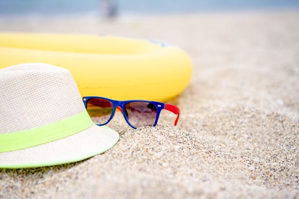 Close-up of summer beach essentials, including a straw hat, sunglasses, and inflatable on sandy beach.