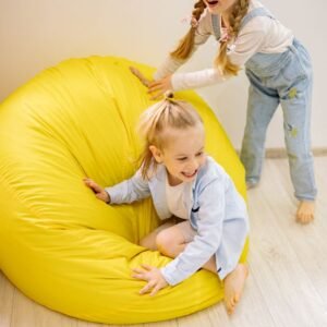 Two happy children playing on a bright yellow bean bag indoors, enjoying fun and laughter.