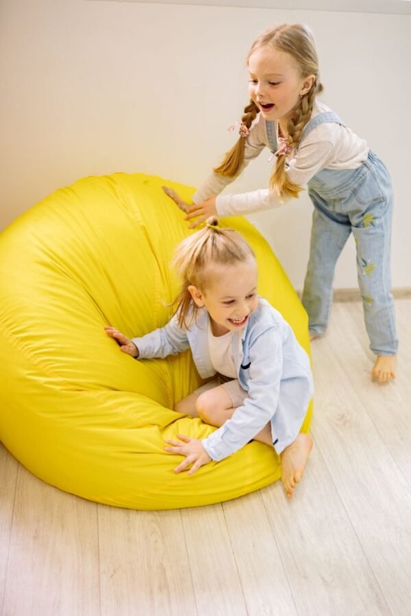 Two happy children playing on a bright yellow bean bag indoors, enjoying fun and laughter.