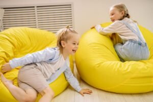 pexels-photo-8612875-8612875 Two young girls having fun on yellow bean bags indoors, embracing joy and leisure.