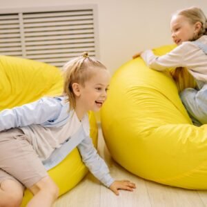 Two young girls having fun on yellow bean bags indoors, embracing joy and leisure.